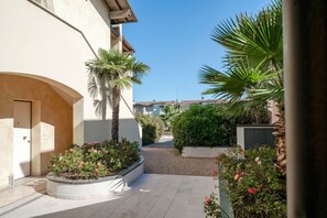 A courtyard with a curved pathway, palm trees, and flower beds. - Sisy by the Lake—with Wi-Fi, a pool, and a garage (Sirmione)