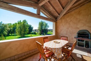 A covered patio with a table and chairs, a grill, and a view of a green landscape. - Sisy by the Lake—with Wi-Fi, a pool, and a garage (Sirmione)