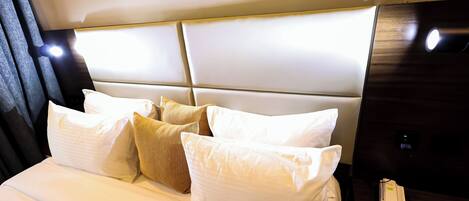 Una habitación de hotel con una cama grande, varios almohadones, una mesita de noche con teléfono, y una lámpara de pared.