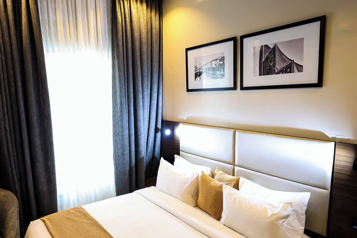 A hotel room with a large bed, a bedside table, a chair, and a window with curtains.