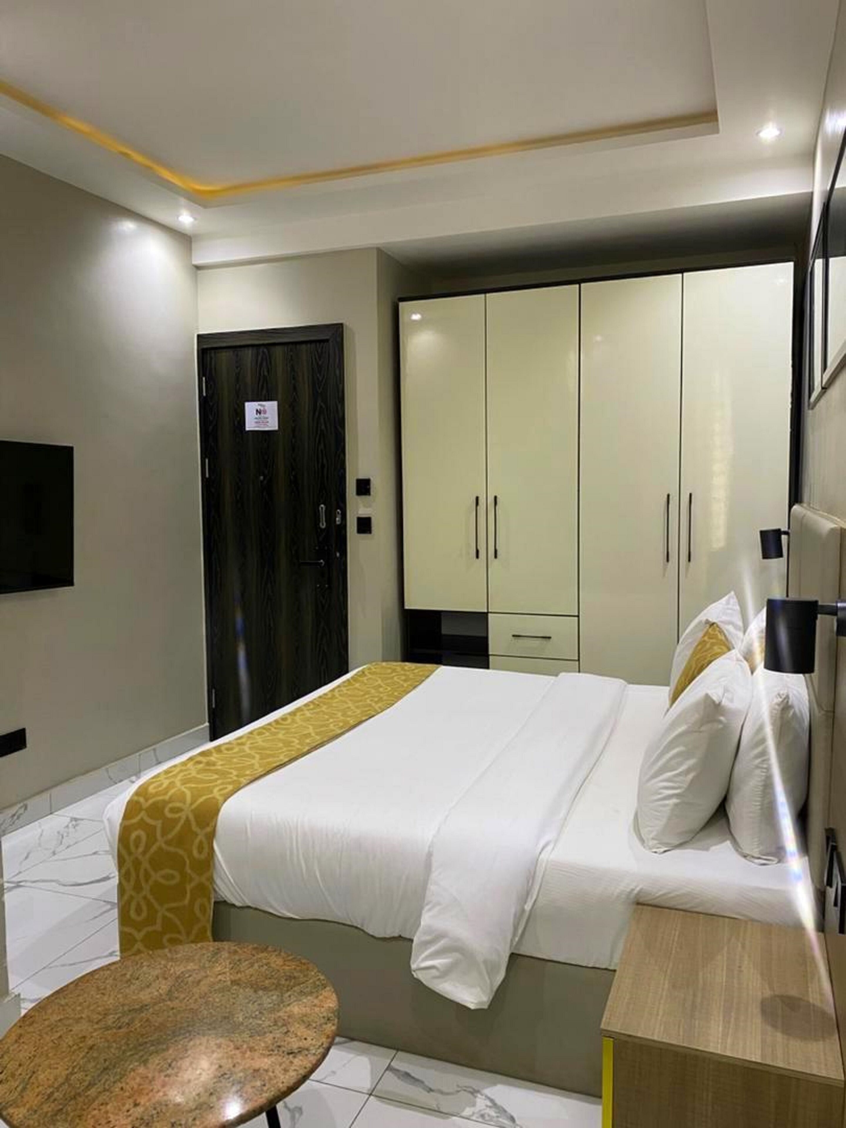 Una habitación de hotel moderna con una cama, una mesita redonda pequeña, un armario y un televisor montado en la pared.