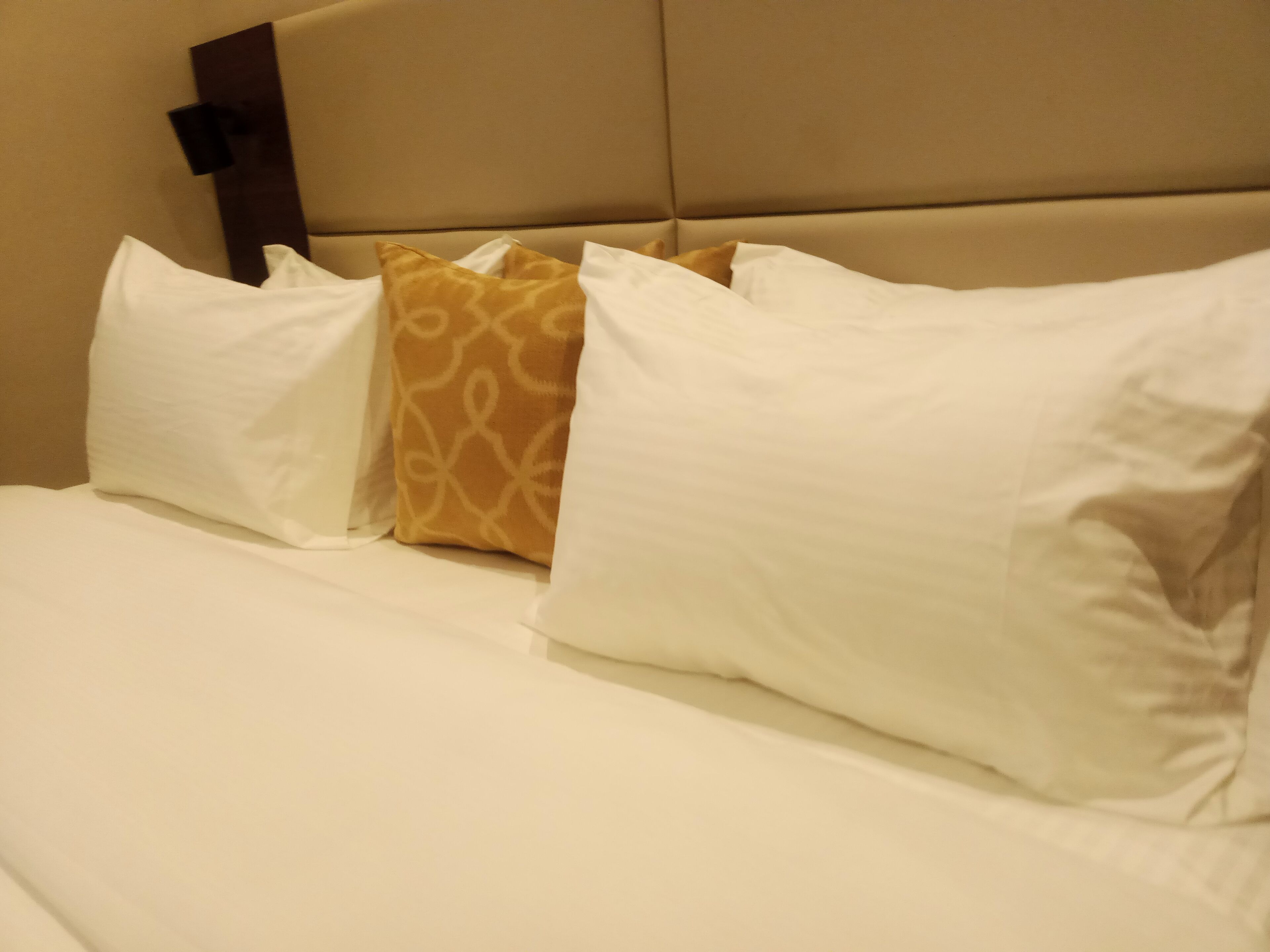 Una cama con almohadas blancas y estampadas, un cabecero y un detalle en marrón.