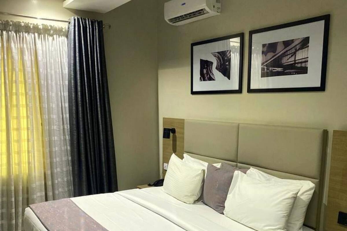 A hotel room with a large bed, a nightstand, a small round table, and two framed pictures on the wall.