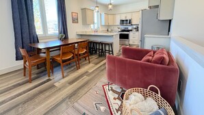 Eine moderne Küche mit Kochinsel, Esstisch aus Holz und Stühlen. Ein rotes Sofa und ein gewebter Korb befinden sich auf dem Boden.