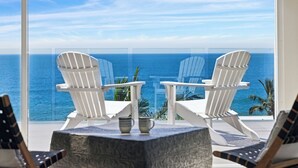Two white Adirondack chairs facing a large window overlooking the ocean. - Epicview - Incredible views, Pets stay free (SAPPHIRE BEACH)