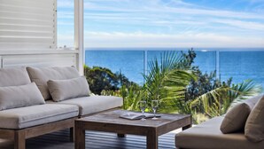 A balcony with a sofa and a coffee table, overlooking a scenic ocean view with palm trees. - Epicview - Incredible views, Pets stay free (SAPPHIRE BEACH)