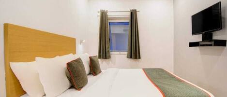 A hotel room with a bed, a television mounted on the wall, and a window with curtains.