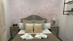 A neatly made bed with a headboard, two bedside tables with lamps, and a wall-mounted shelf with a plant. - VTZ The Botanic Hostel (Zaragoza)