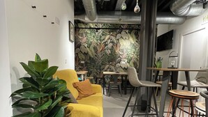 A modern interior with a yellow sofa, dining area, and a large plant. - VTZ The Botanic Hostel (Zaragoza)
