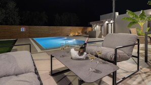 An outdoor patio with a pool, lounge chairs, and a table with a bottle of champagne. - Melia Villa in Kolympia (Kolympia)