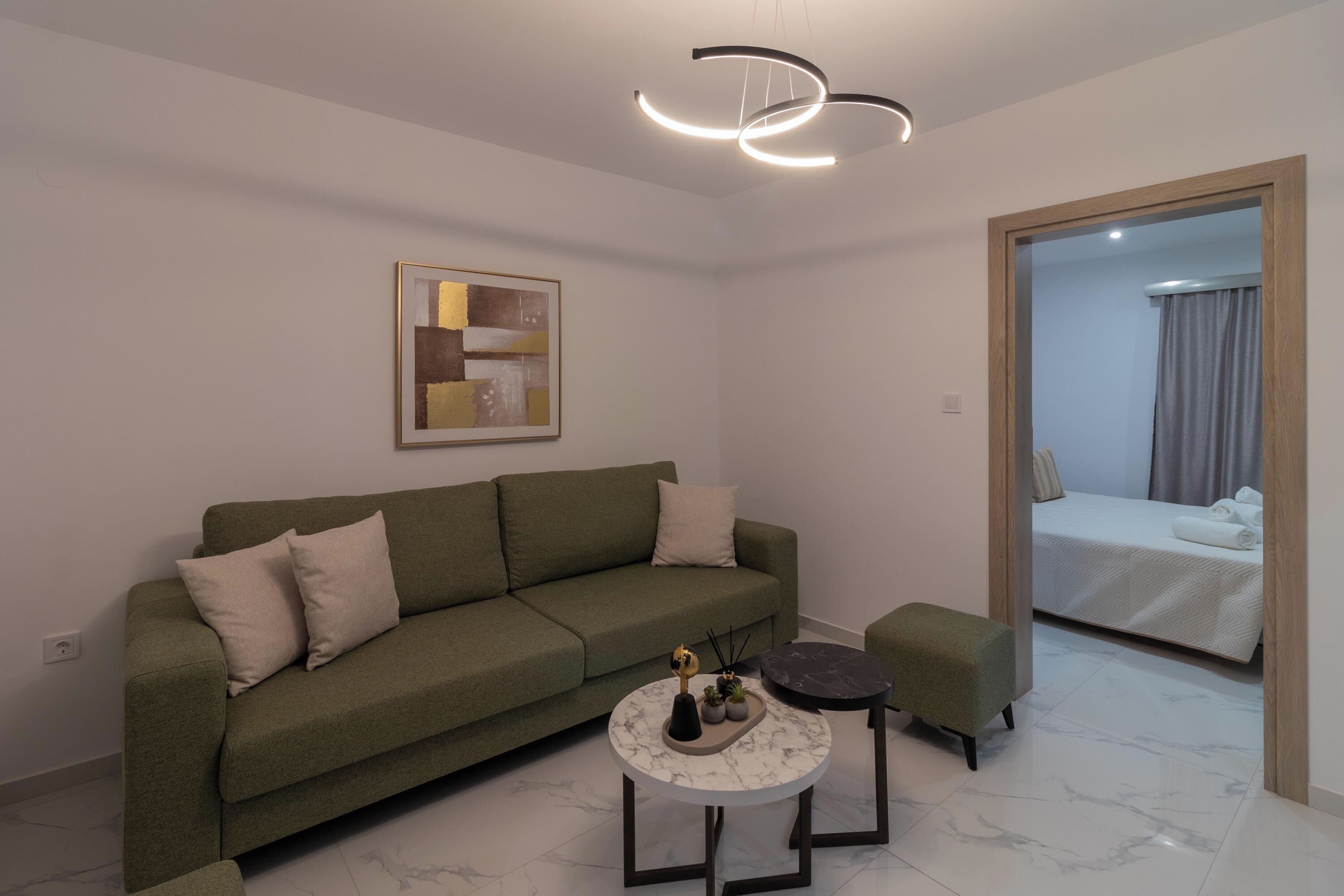 Un salon moderne avec un canapé vert, une table basse ronde et un lit dans la pièce adjacente.