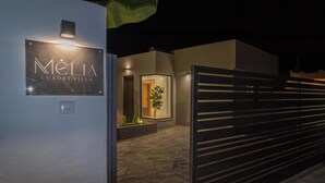 A modern villa entrance with a sign reading 'MELIA LUXURY VILLA,' a stone pathway, and a gated area. - Melia Villa in Kolympia (Kolympia)