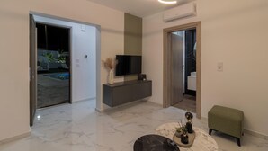 A modern living room with a flat-screen TV on a grey console, a marble floor, and a green upholstered stool. - Melia Villa in Kolympia (Kolympia)