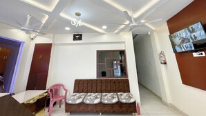 A living room with a sofa, a television mounted on the wall, ceiling fans, recessed lighting, and a security camera. - Hotel Gupta Residency - near Temple  (Ujjain)