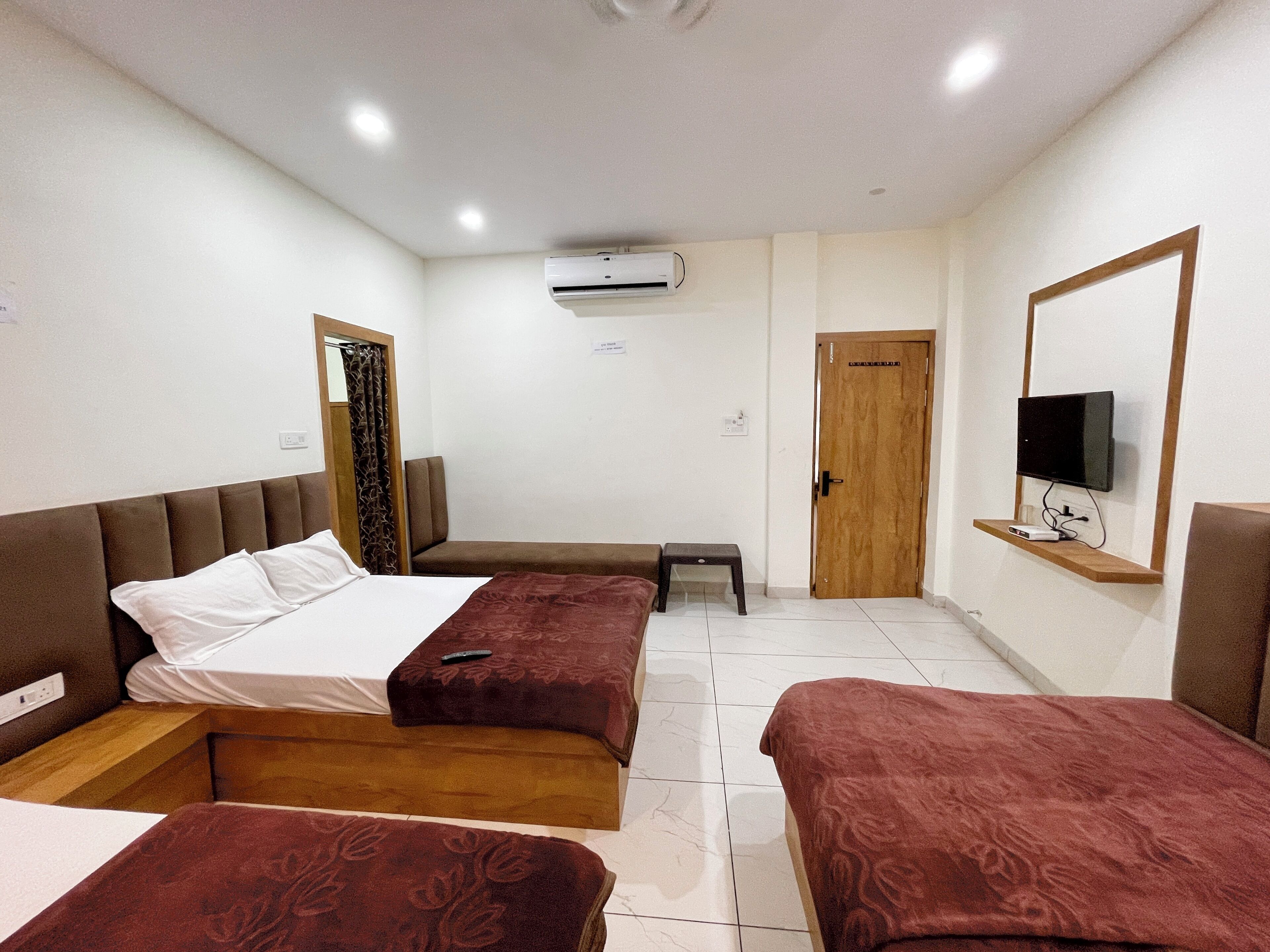 A hotel room with two beds, a TV, an air conditioner, a small table, and a door.