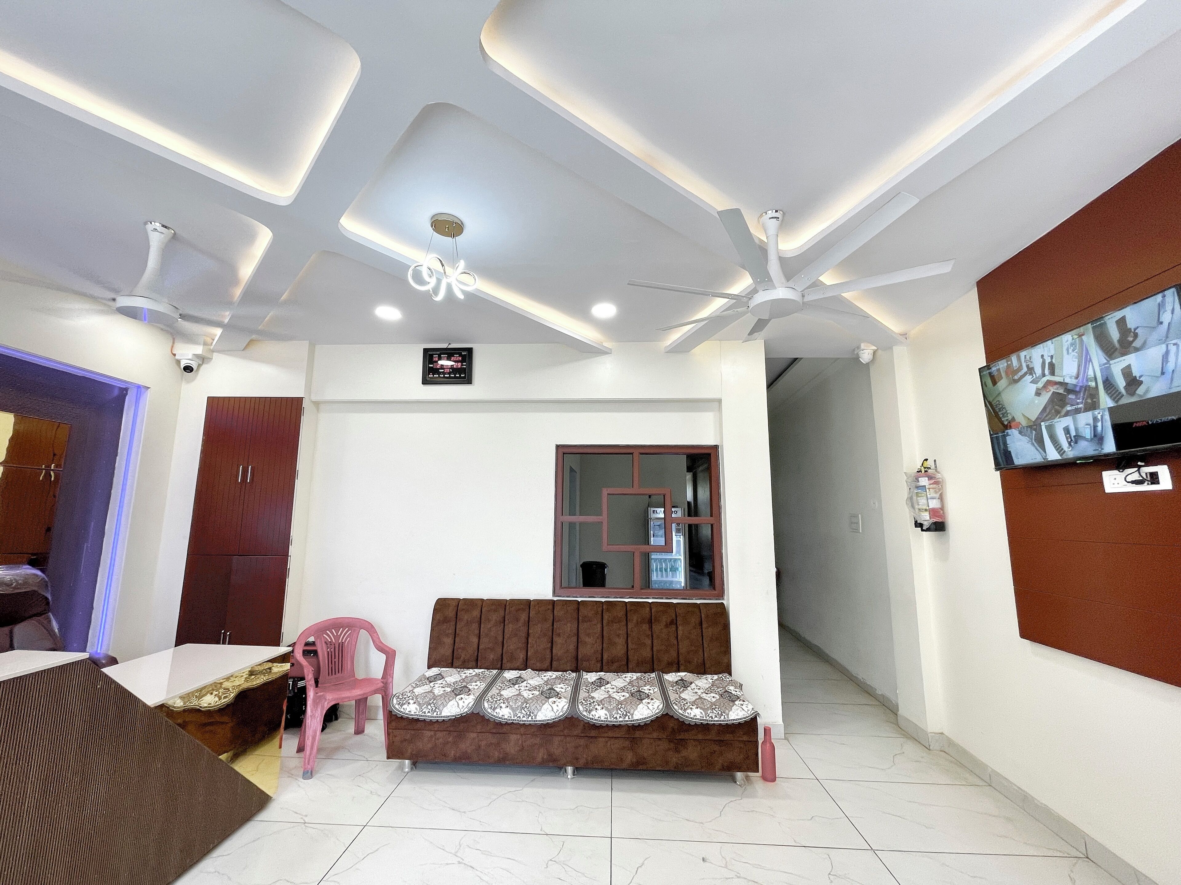 A modern living room with a brown sofa, a pink chair, a TV mounted on the wall, and ceiling fans.