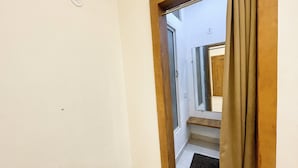 A narrow hallway with a wooden door frame, a small rug at the bottom, and a light switch on the wall. - Hotel Gupta Residency - near Temple  (Ujjain)
