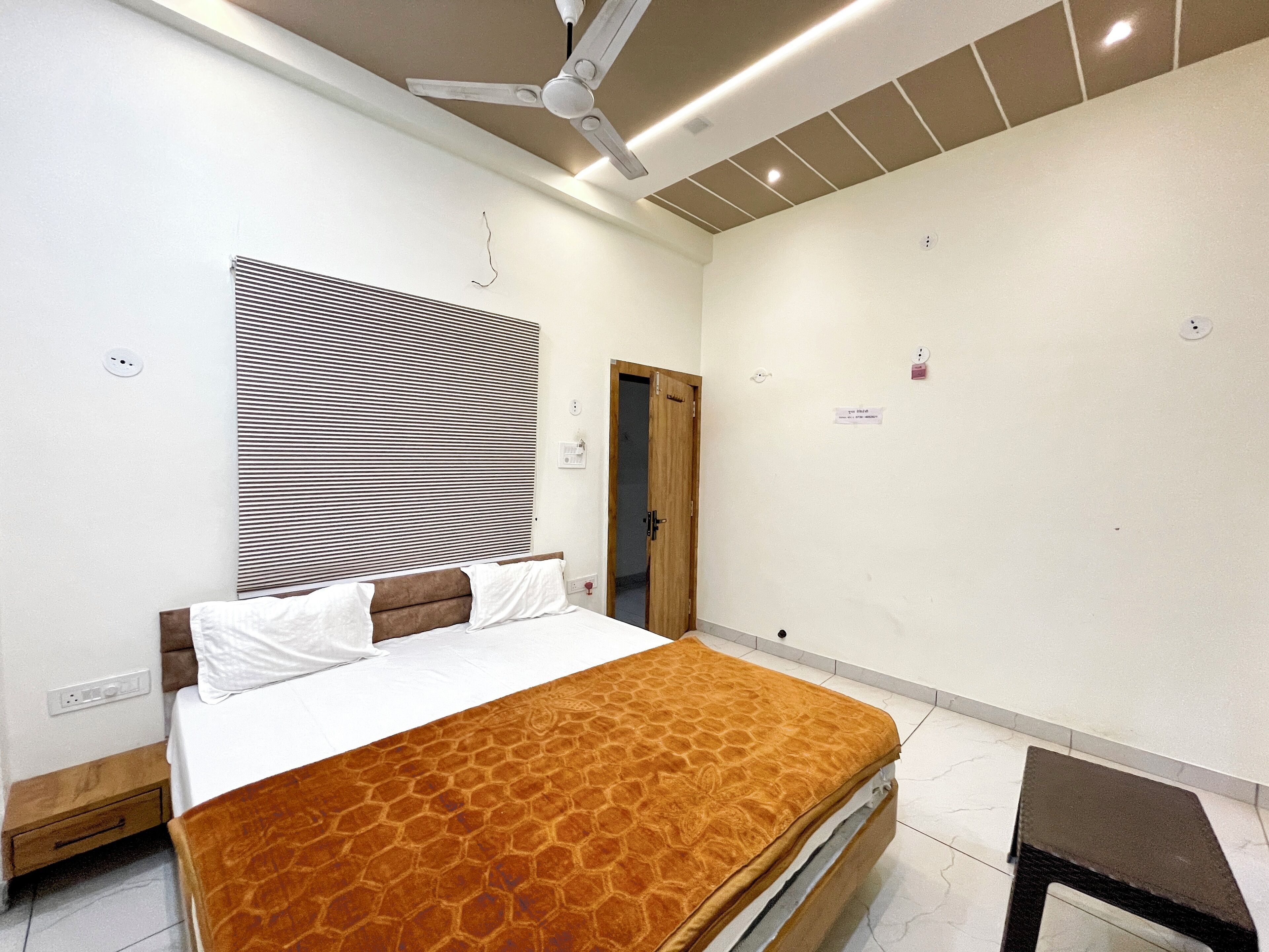 Ein Schlafzimmer mit Bett, Deckenventilator, Fenster mit Jalousien, einer Tür und einem kleinen Tisch.