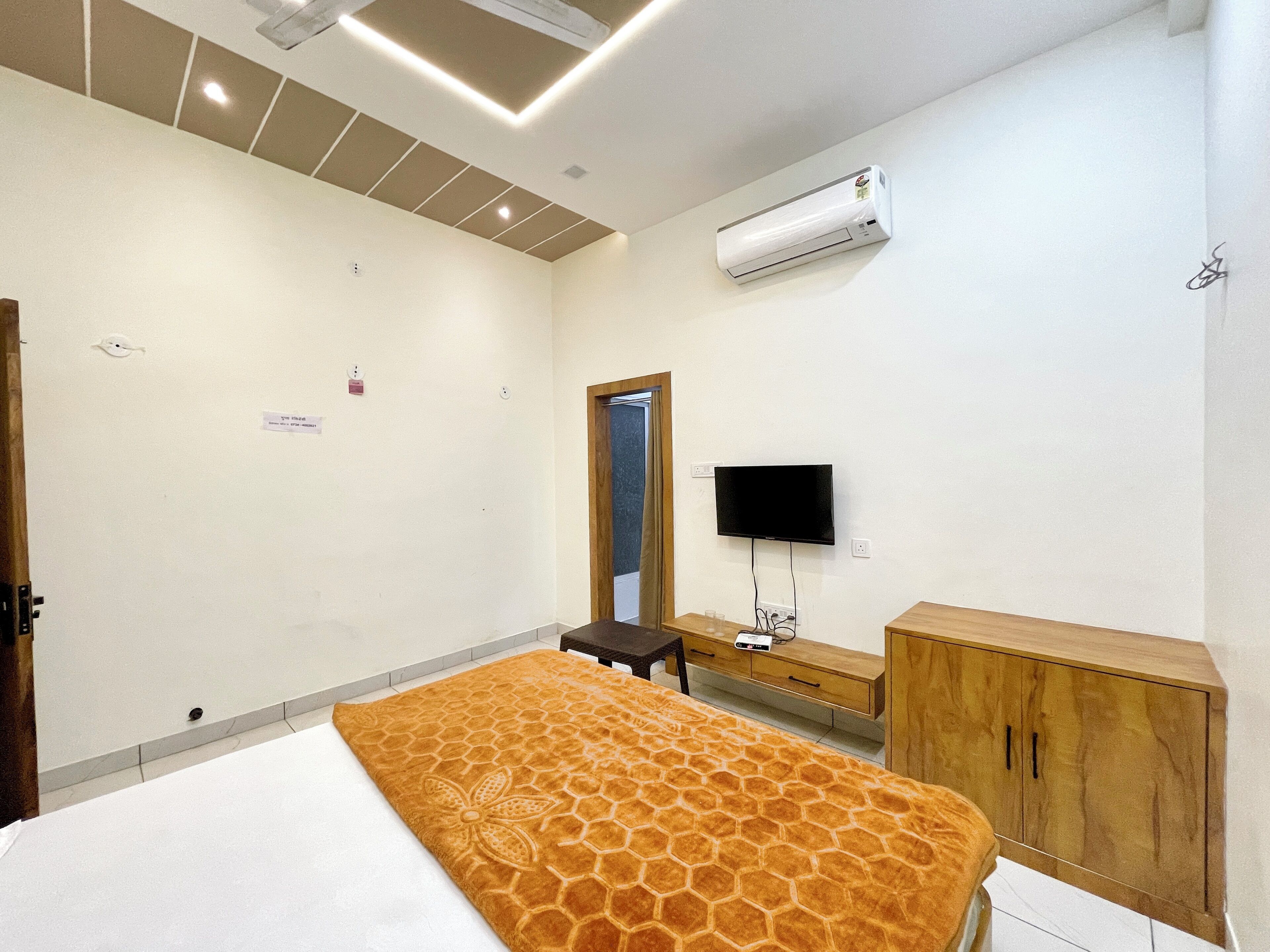 A hotel room with a bed, a TV, an air conditioner, a wooden cabinet, and a small table.
