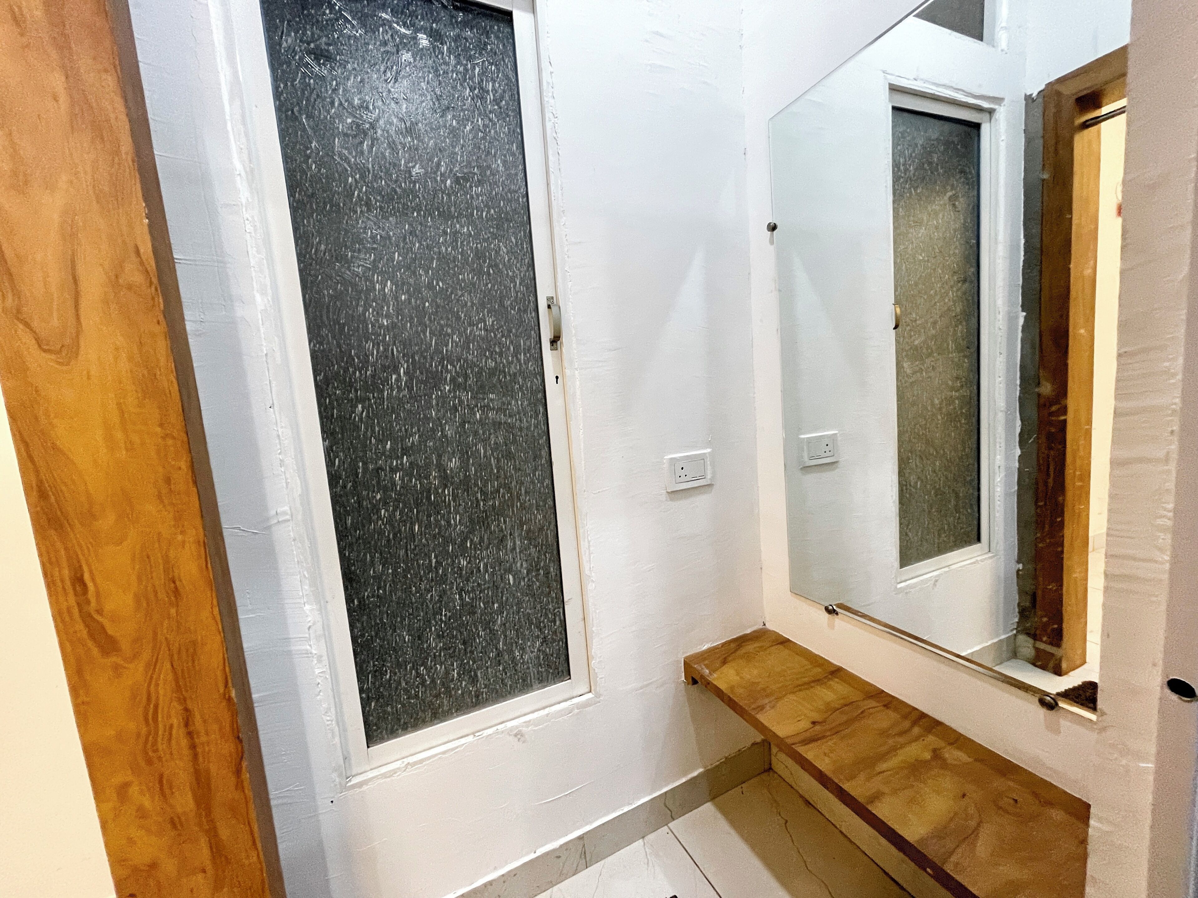 Un baño con pared blanca, banca de madera y espejo.