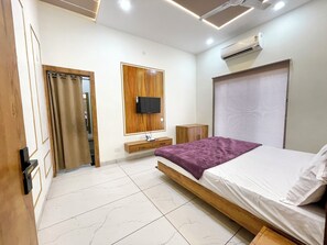 Un dormitorio moderno con estructura de cama de madera, televisor de pantalla plana montado en un panel de madera, una mesita de noche y una ventana con persianas.