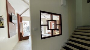 A hallway with a staircase, a wall-mounted TV, and a window with a geometric frame. - Hotel Gupta Residency - near Temple  (Ujjain)