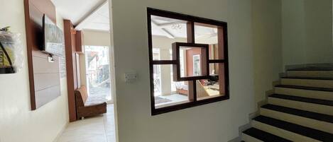 Un pasillo con una escalera, un televisor montado en la pared y una ventana con un marco geométrico.