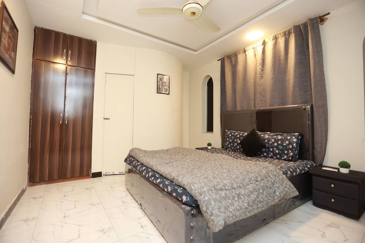 Une chambre à coucher comprenant un lit, une armoire, une table de chevet et un ventilateur de plafond.