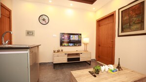 A compact hotel room with a kitchenette, a wooden cabinet, a flat-screen TV mounted on the wall, a wooden door, and a painting on the wall. - Hotel Dream Heights Hotel and Apartment (Rawalpindi)