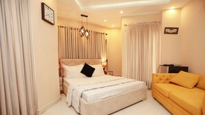 A bedroom with a bed, a sofa, curtains, a clock, and a lamp. - Hotel Dream Heights Hotel and Apartment (Rawalpindi)