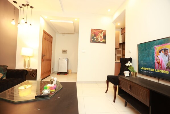A living room with a glass coffee table, a black sofa, a TV on the wall, and a wooden cabinet. - Hotel Dream Heights Hotel and Apartment (Rawalpindi)