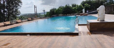 A swimming pool with a wooden deck, benches, and a statue.