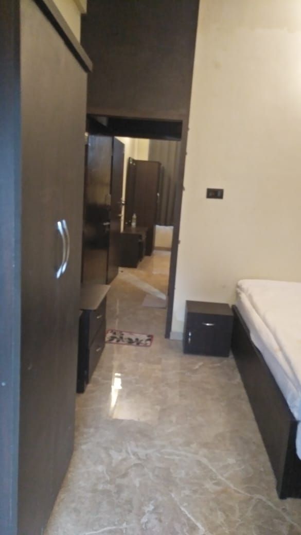 A narrow hallway with a bed on the right, a wardrobe on the left, and a door at the end leading to another room.