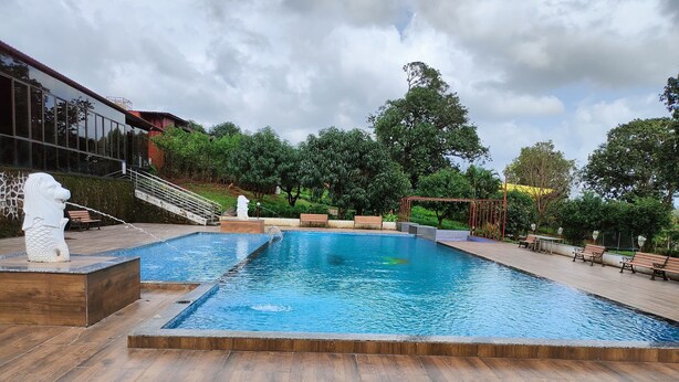 Una piscina rectangular con un deck de madera que la rodea, bancos a lo largo del borde y una estatua de un león.