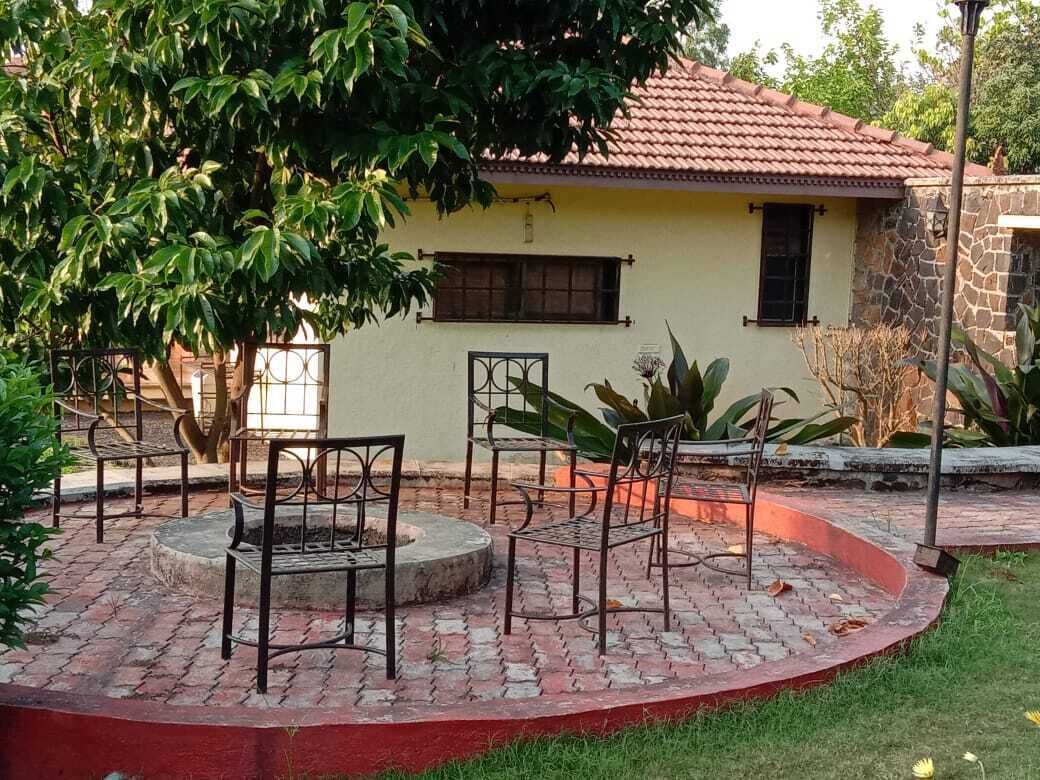 A courtyard with a circular brick seating area, a stone wall, and a building with a tiled roof.