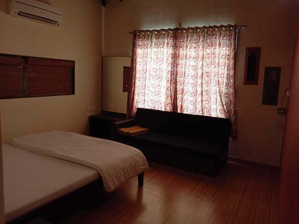 Una habitación pequeña y con poca luz, con una cama, un sofá y una ventana con cortinas estampadas.