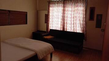 Una habitación pequeña y con poca luz, con una cama, un sofá y una ventana con cortinas estampadas.