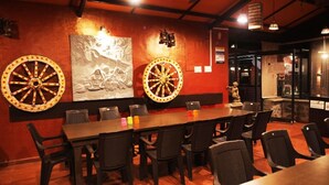 Un restaurante con una larga mesa de madera y sillas negras, decorado con dos ruedas grandes y elaboradas en la pared.