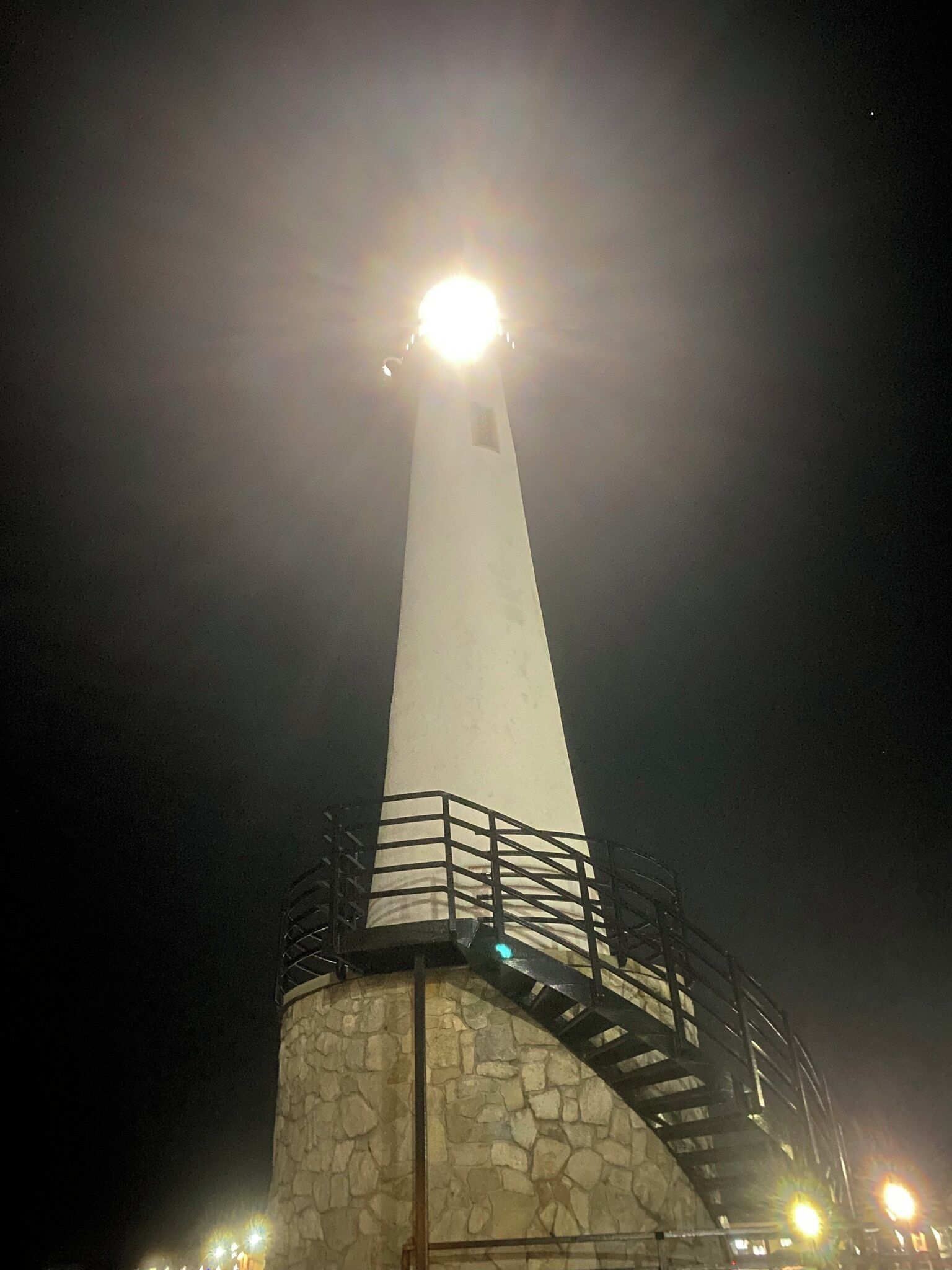 A tall, white lighthouse with a stone base and a metal railing around the top.
