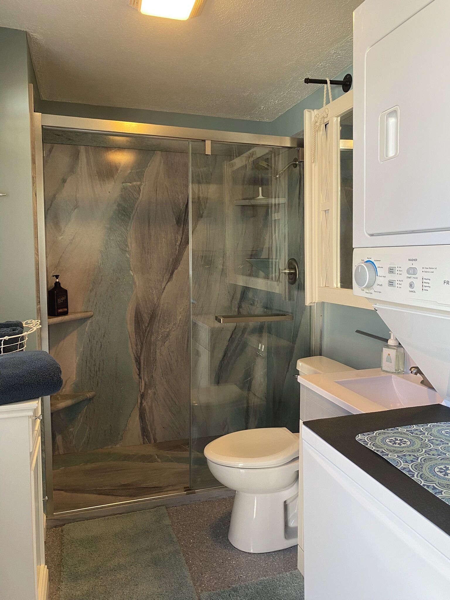 Une salle de bain avec une douche à parois de verre, des toilettes blanches et un lavabo doté d’un plan de travail à motifs.