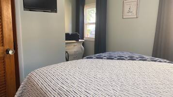 A bedroom with a bed, a dresser, a TV mounted on the wall, and a window with curtains.