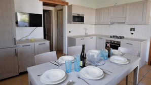 A modern kitchen with white cabinets, a built-in oven, and a dining area set for six with white plates and blue glasses. - Luisa Apartment In Budoni Shared Pool (Budoni)