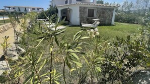 A modern house with a stone facade, a covered patio with lounge chairs, and a well-maintained garden. - Luisa Apartment In Budoni Shared Pool (Budoni)