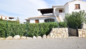 A two-story house with a stone wall entrance, a covered porch, and a tiled roof. - Luisa Apartment In Budoni Shared Pool (Budoni)