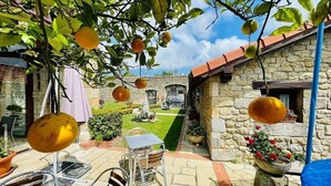 A stone building with a tiled roof, a small garden with a lawn, and a table and chairs in the foreground. - POSADA LA VICTORIA (Miengo)