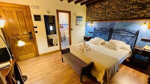 A cozy bedroom with a wooden floor, a bed with white linens, a bench, a wooden door, and a stone wall. - POSADA LA VICTORIA (Miengo)