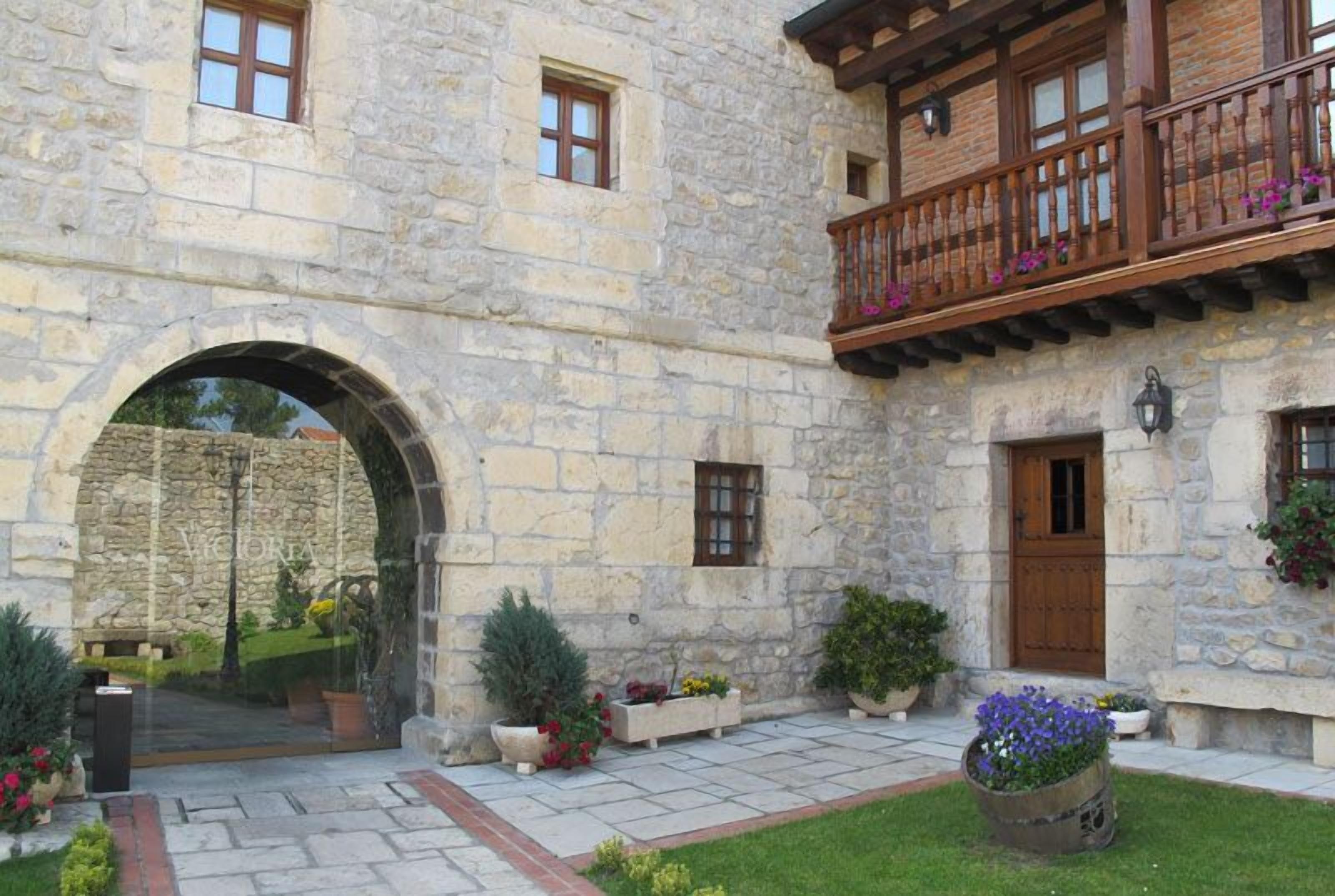 Ein Steinhaus mit einem hölzernen Balkon, einem Rundbogen-Eingang und Kübelpflanzen.