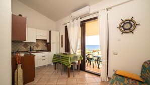 Une cuisine compacte avec un coin repas, un canapé et une vue sur la mer grâce à une porte vitrée.