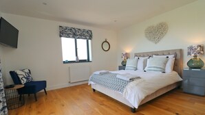 Une chambre avec un grand lit, un téléviseur fixé au mur, une fenêtre avec un rideau et un élément décoratif en forme de cœur sur le mur.