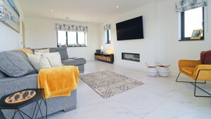 Un salon moderne avec un canapé gris, un fauteuil jaune, un téléviseur à écran plat et une cheminée.